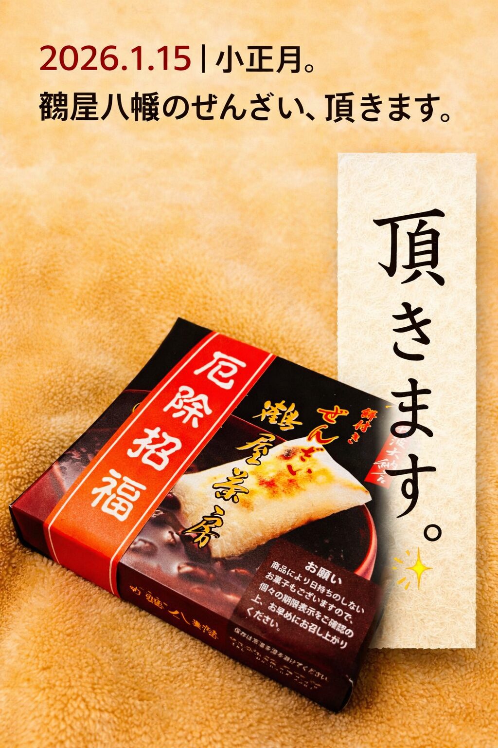 2026年1月15日の小正月に、鶴屋八幡のぜんざいを頂く様子。赤と黒のパッケージのぜんざいが、やわらかなベージュの布の上に置かれている。